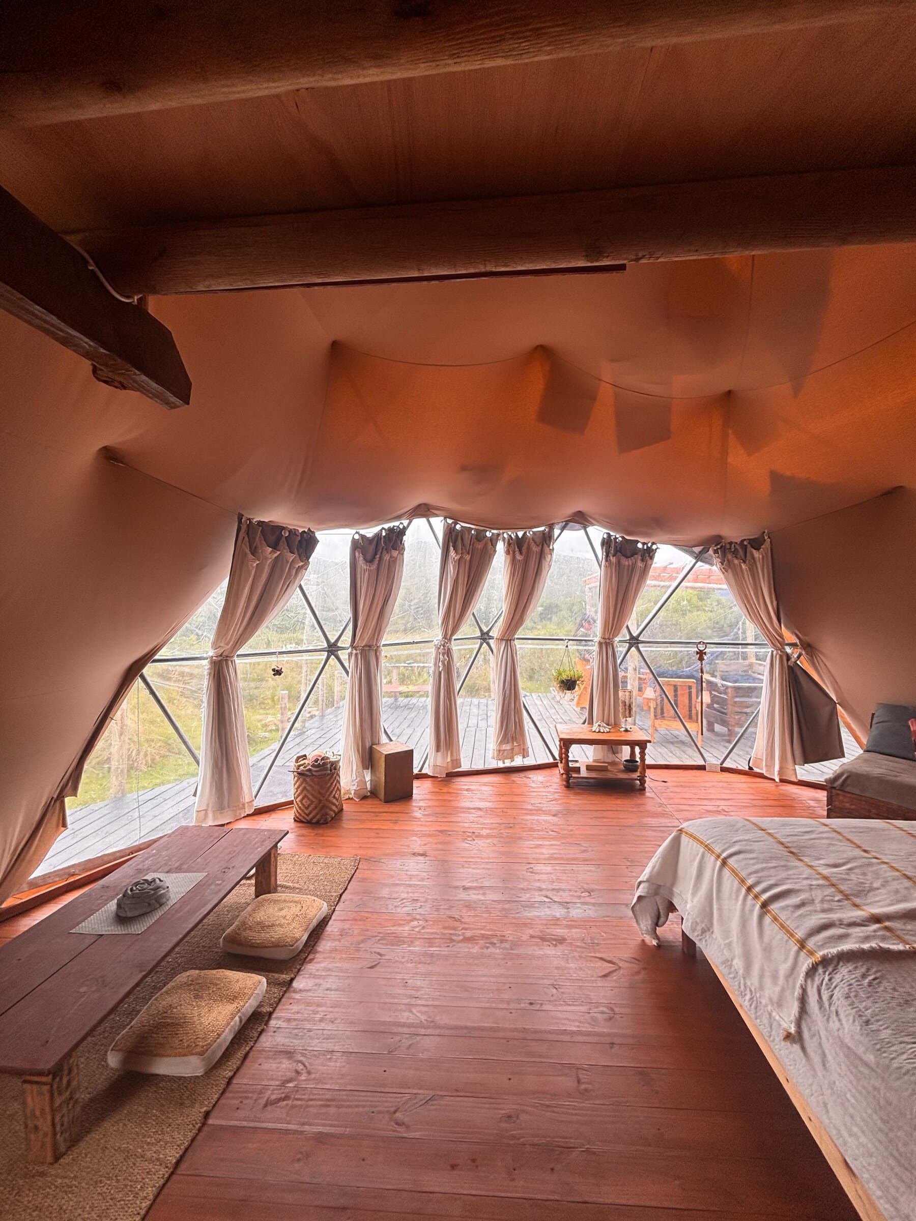 Interior del domo con la cama y la pared de vidrio abierta al campo
