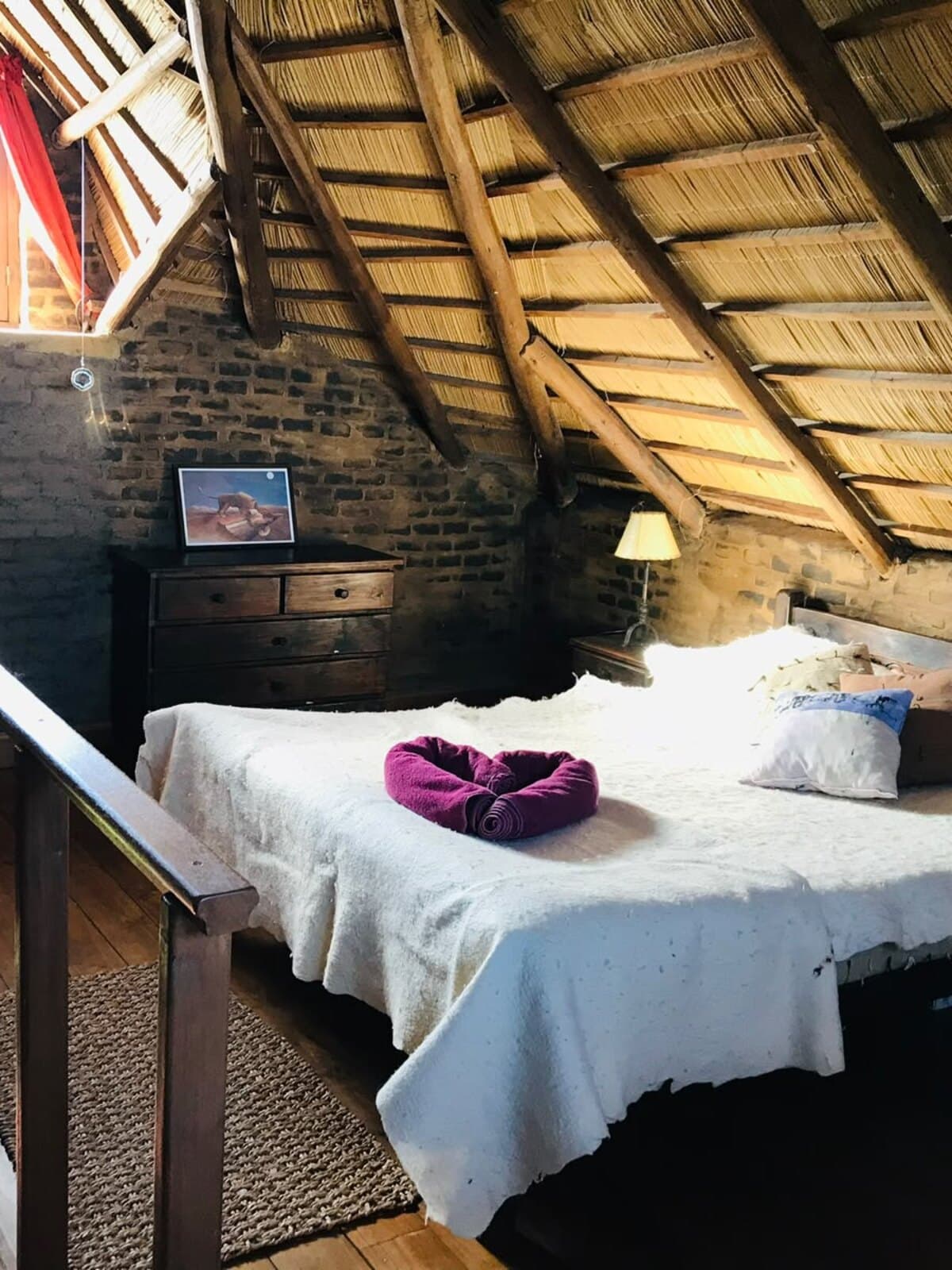 Cuarto de la posada con cama blanca bajo el techo de paja y los muros de piedra