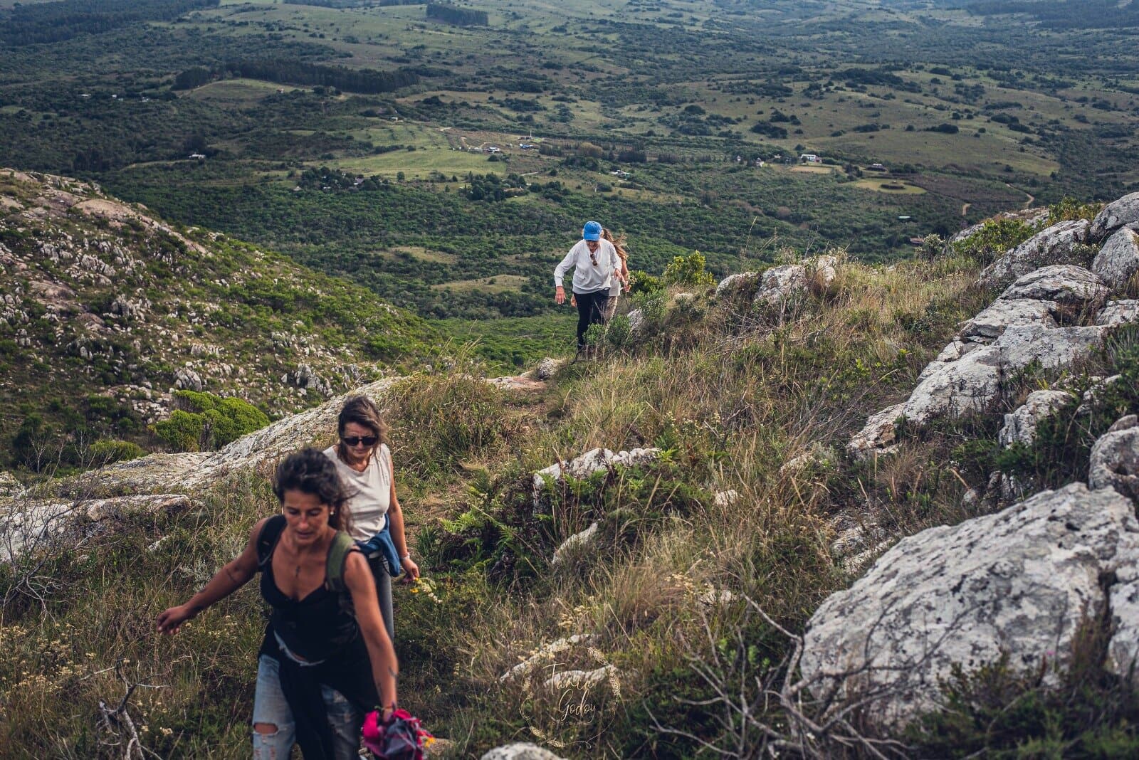 Dos caminantes subiendo entre las rocas de la sierra, con el valle abierto abajo