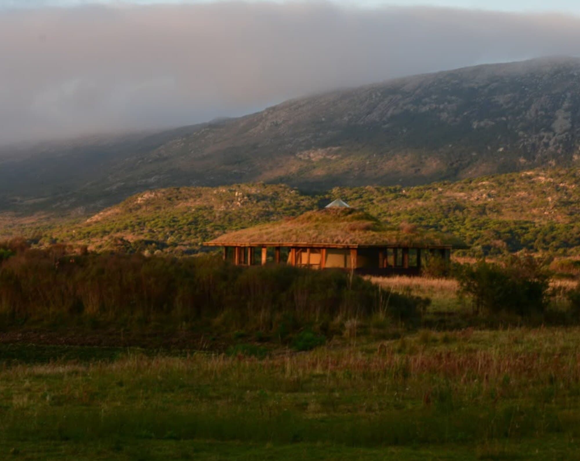 El templo de techo de pasto al amanecer, con la niebla bajando por la sierra detrás