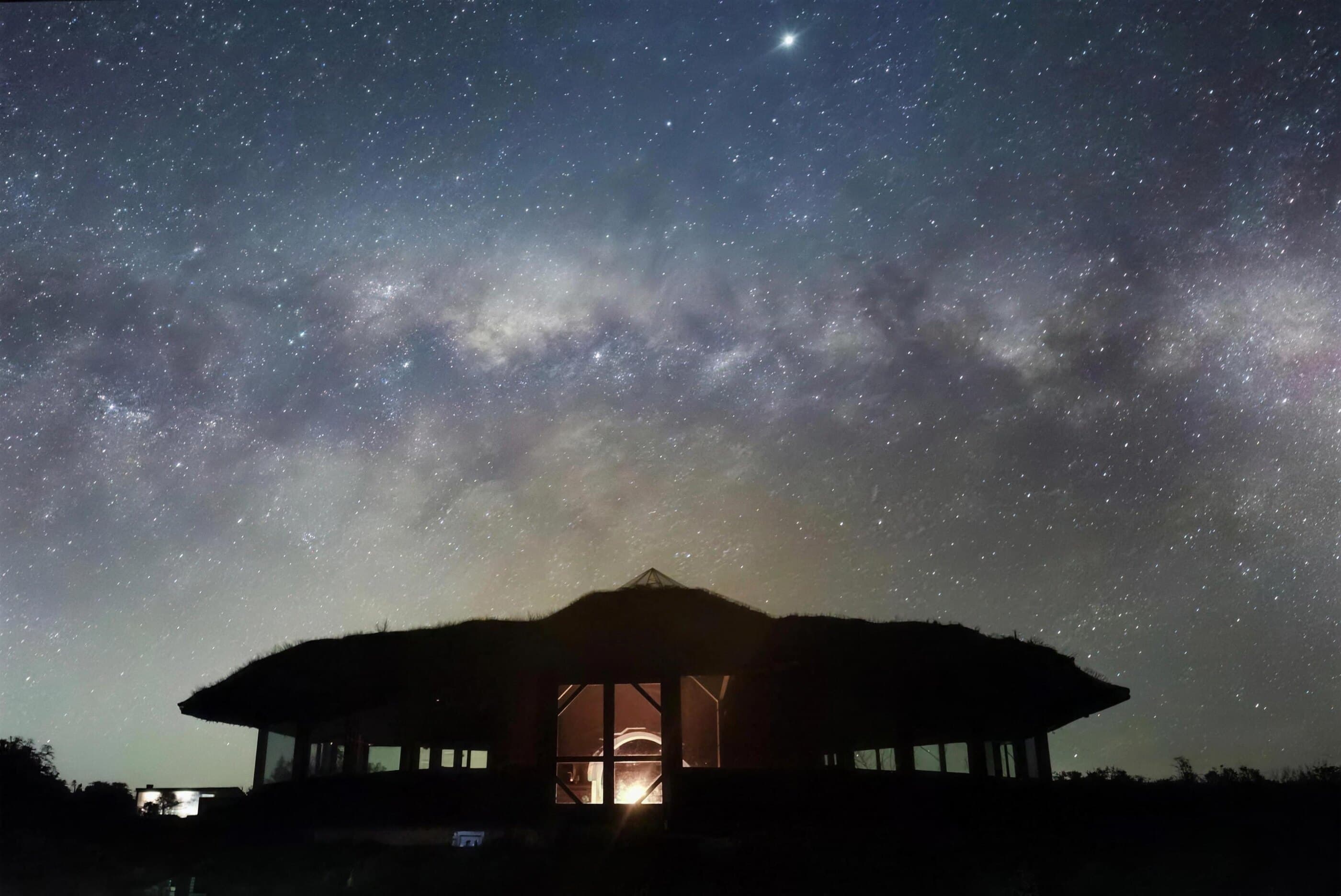 El templo de la base recortado contra la Vía Láctea, con luz cálida saliendo por sus aberturas
