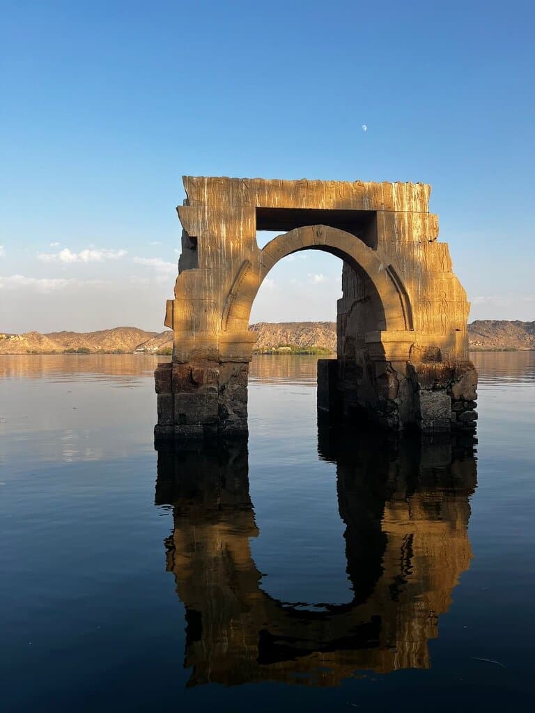 Arco de piedra del templo de Philae reflejado en el agua quieta