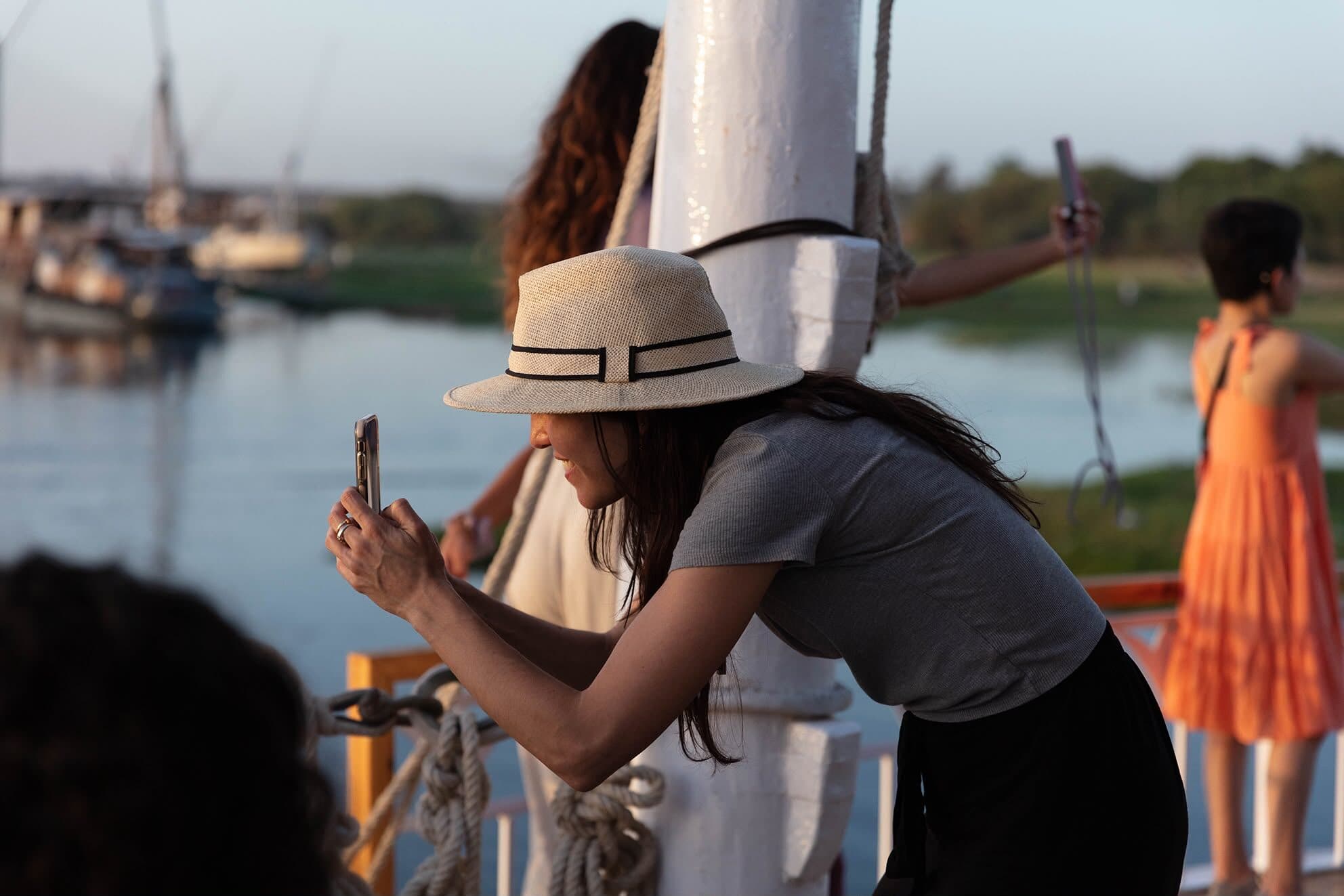 Viajera con sombrero sacando una foto desde la cubierta, con el Nilo detrás