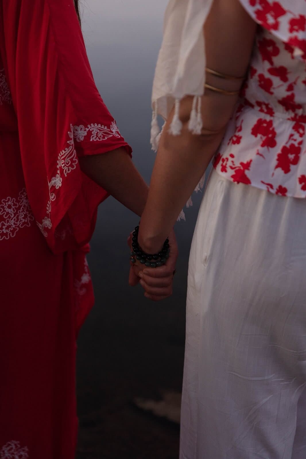 Dos viajeras de la mano, una de rojo y otra de blanco, al anochecer