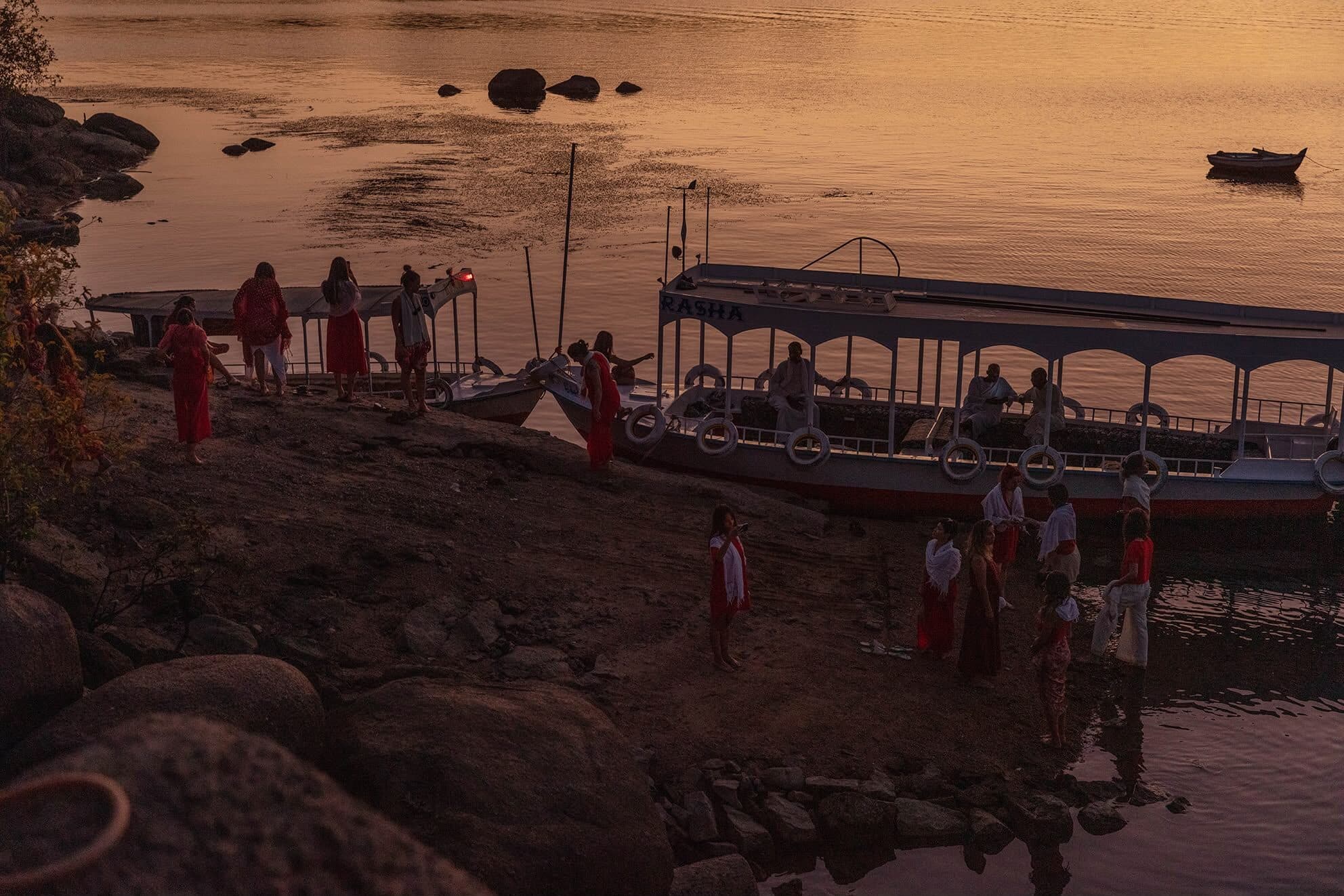 El grupo en la orilla del Nilo junto a la barca, con el agua encendida por el atardecer