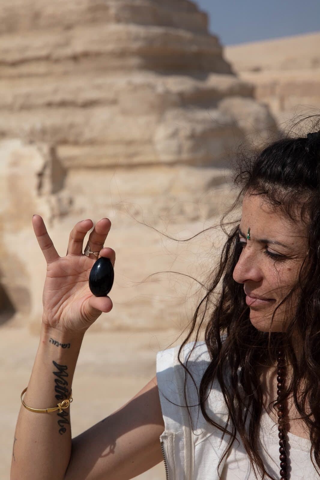 Viajera sosteniendo una piedra oscura a contraluz frente a la roca del templo