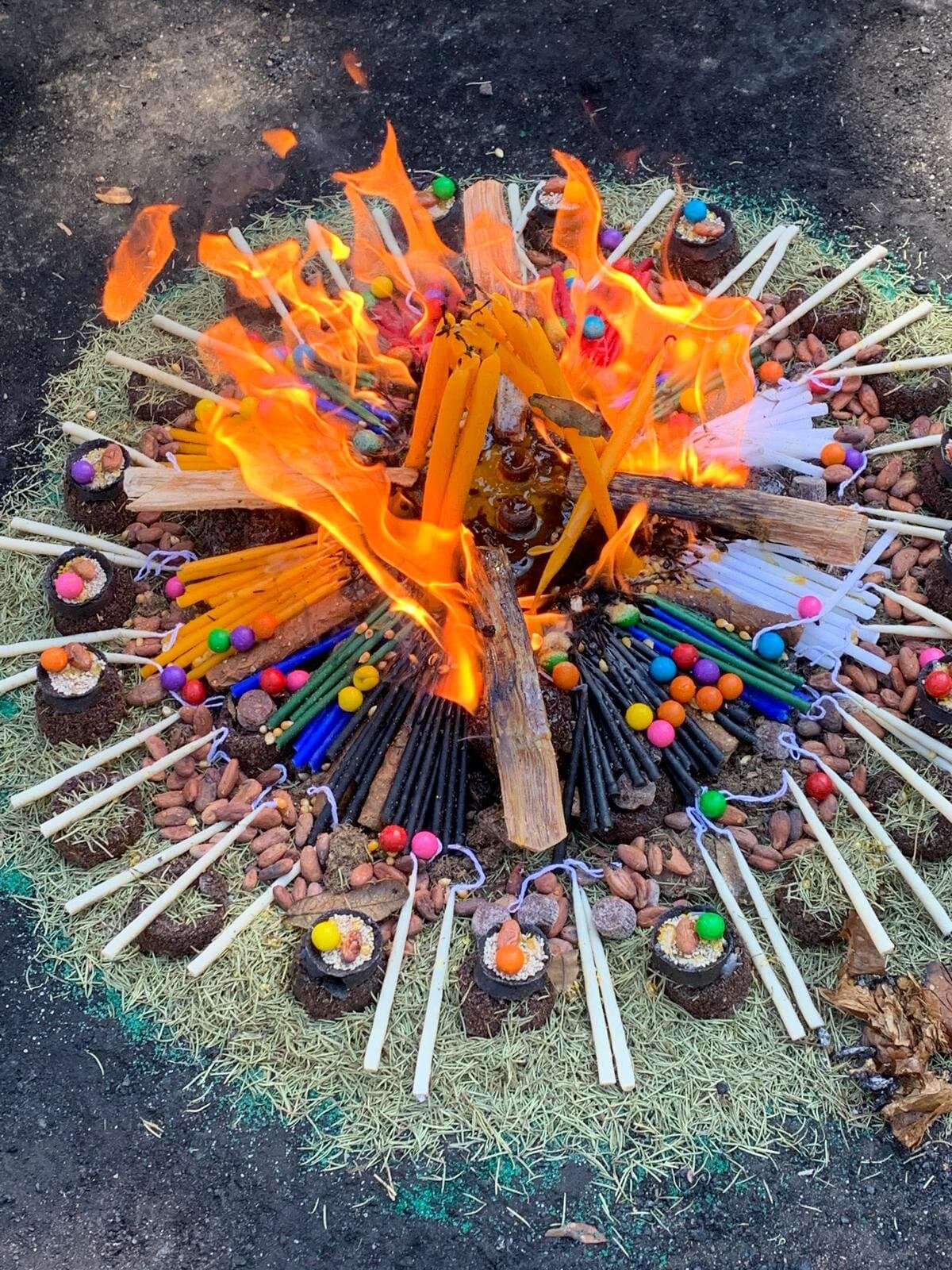 Mandala ceremonial de velas de colores, copal y cacao ardiendo sobre la tierra