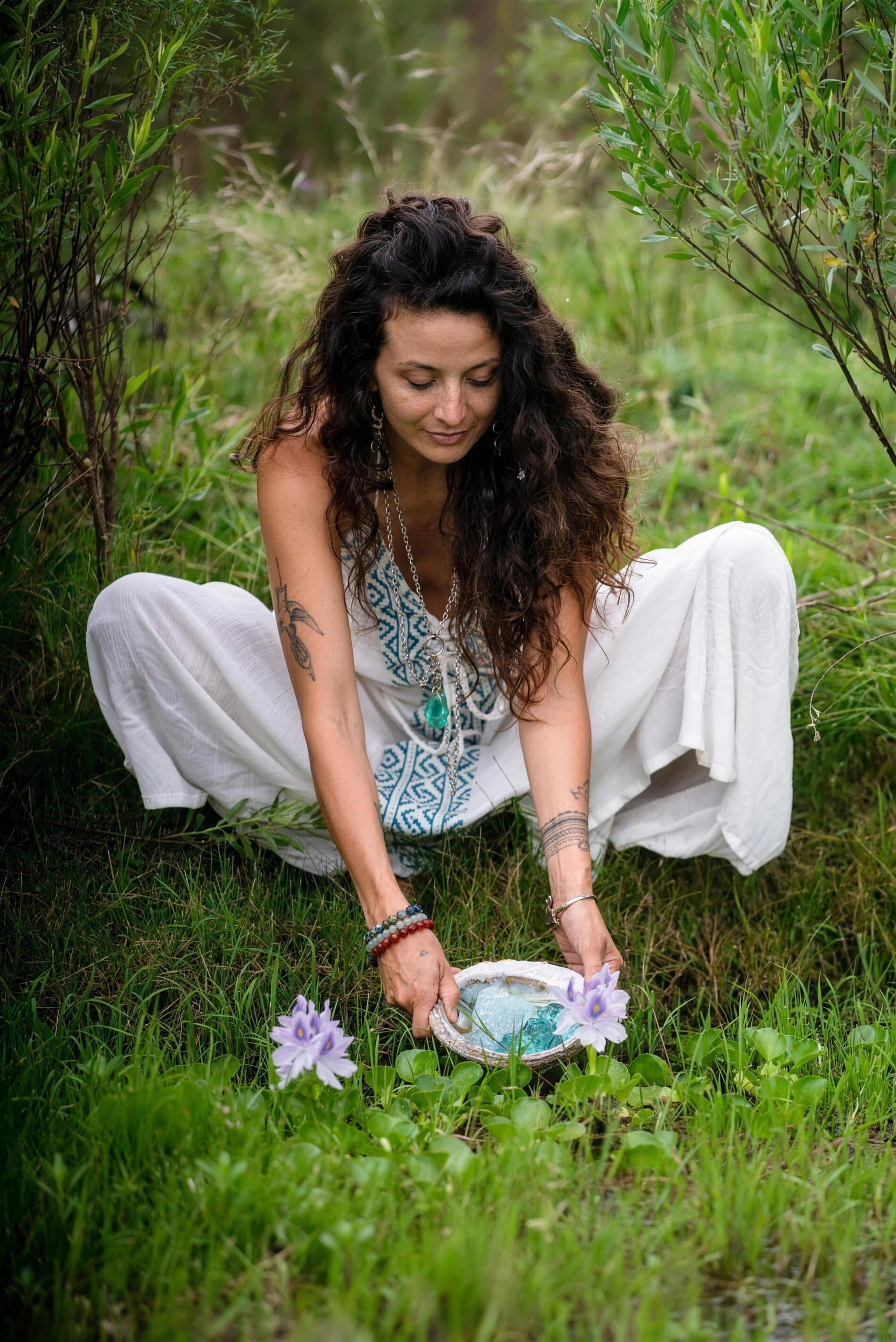 Mujer sentada en el pasto apoyando un cuenco con flores de loto sobre la tierra